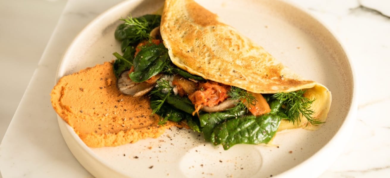 Savory omelette filled with fresh spinach, mushrooms, and herbs, served on a plate with a side of red pepper hummus.